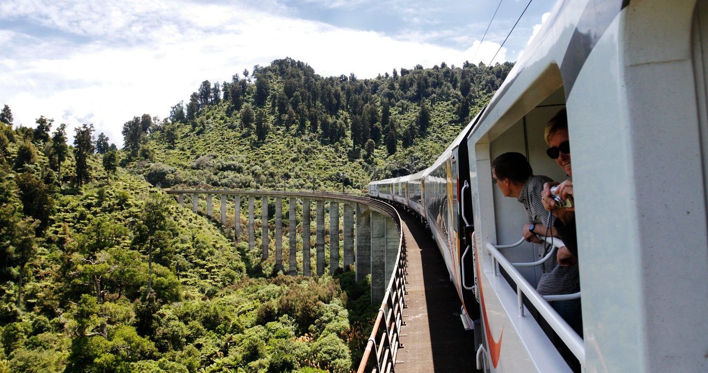 Image of Two passengers looking out from inside the open coach of Northern Explorer Train in New Zealand.