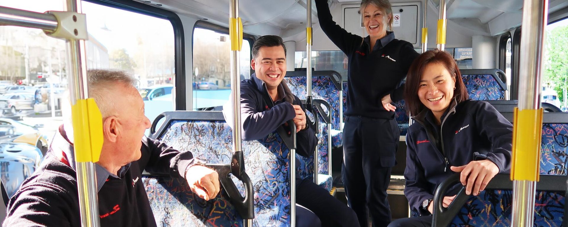 Four bus drivers stand inside a bus and smile at the camera